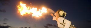 A woman breathes fire at a luau with the coast in the background