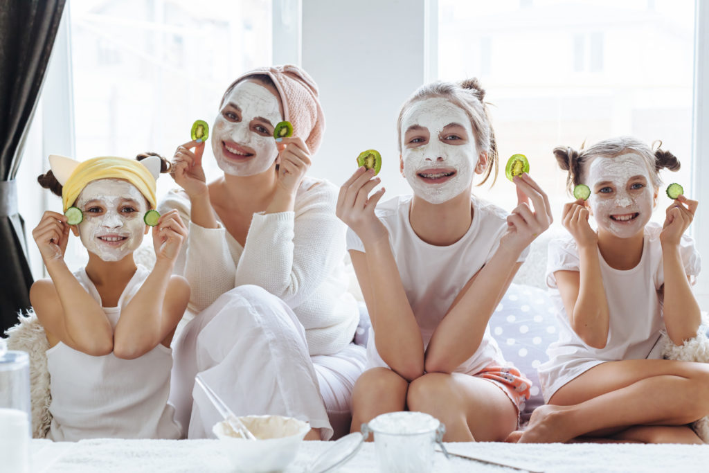 Mom with her daughters making clay face mask. Mother with children doing beauty treatment together. Morning skin care routine.