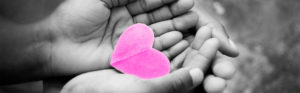 black and white photo of hands with pink paper heart in hands
