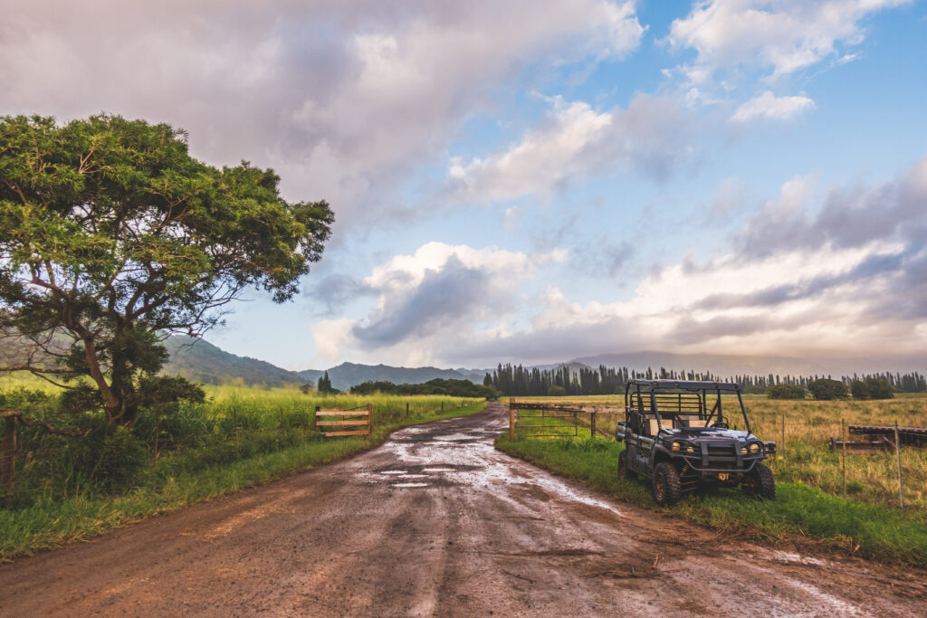 scenic view of tropical landscape with clouds and sky just after the rain. Dirt road with all terrain vehicle parked along side.